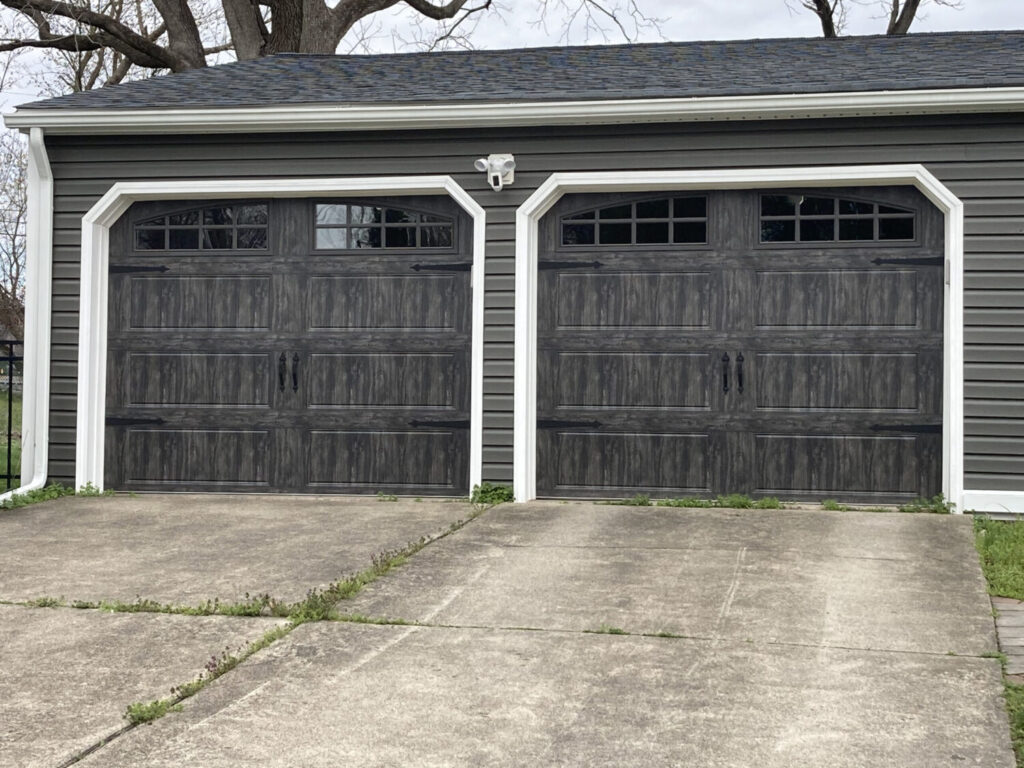 A couple of black garage doors in front of a house.